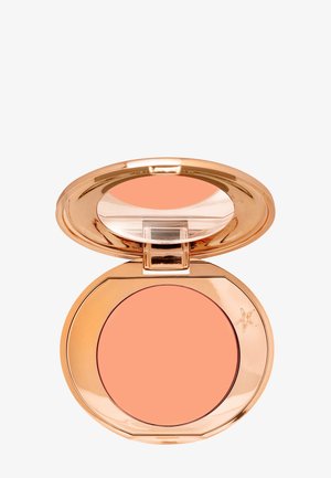 Compact en or rose contenant un fard à joues crémeux de couleur pêche. Le couvercle présente une section transparente. Le compact a une forme octogonale.
