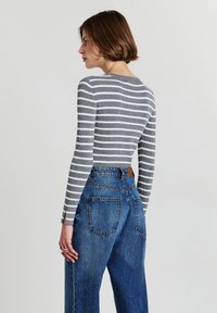 Grau und weiße gestreifteLangarmbluse mit figurbetontem Schnitt, kombiniert mit hochgeschnittenen blauen Denim-Jeans im klassischen Fünf-Taschen-Stil.