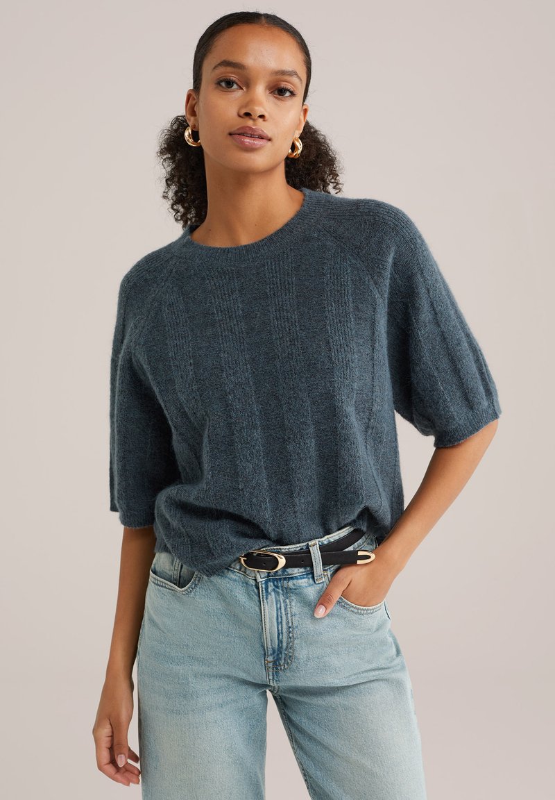 Suéter corto de manga corta de textura azul oscuro con un escote redondeado, combinado con unos vaqueros de lavado claro y un cinturón negro con hebilla dorada.