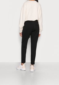 Licht beige cropped sweatshirt, zwarte tapered broek en witte sneakers met lichtroze accenten. Gladde stof met minimale details.