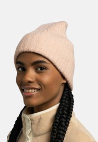 Light pink ribbed knit beanie with a tapered top. Smooth texture, worn with a cream-colored fleece jacket featuring a buttoned collar.