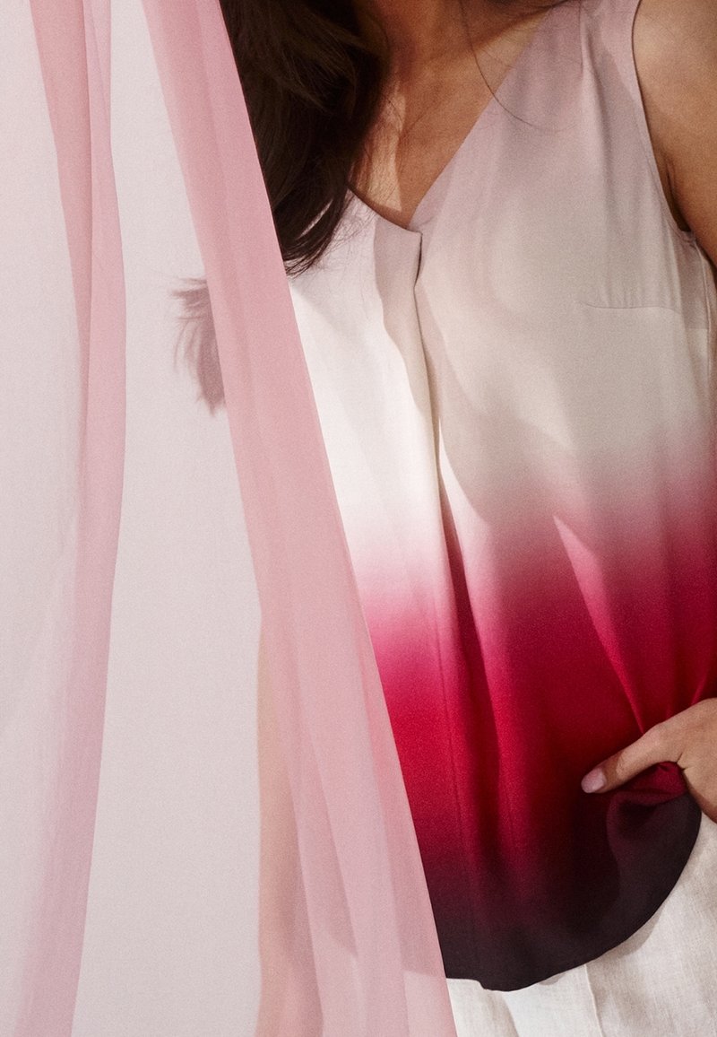 Haut sans manches aux couleurs dégradées, passant d'un beige clair à un rouge profond, avec une texture lisse. Accompagné d'un tissu rose transparent.