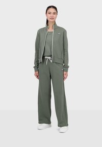 Completo tuta verde oliva composto da giacca con zip e pantaloni con vestibilità comoda e cordoncino in vita, realizzato in tessuto morbido; dettaglio del logo su ciascun pezzo.