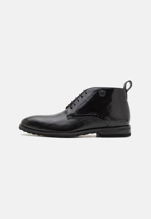 Botas de tobillo de cuero negro con un acabado texturizado, puntera redonda, parte delantera con cordones y un acento de logo en el costado. Suela de goma duradera.