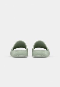 Une paire de sandales légères vert clair à enfiler avec un dos ouvert et "Tommy Jeans" embossé sur le talon, vue de l'arrière.