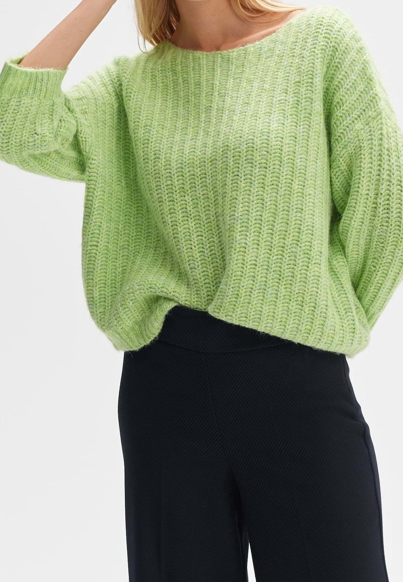 Pull en maille vert citron à coupe ample, col large et texture côtelée. Associé à un pantalon taille haute noir à fines rayures.