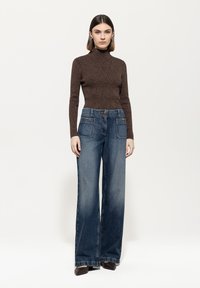 Brauner Langarmrollkragenpullover, kombiniert mit hochtaillierten, weiten Jeans. Die Jeans verfügen über zwei Fronttaschen und einen Knopfverschluss.