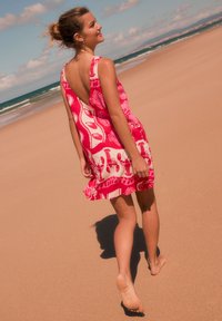 Robe rose sans manches avec un dos en V profond, arborant un motif audacieux de homard et de vagues. Tissu léger et fluide, idéal pour une tenue de plage.