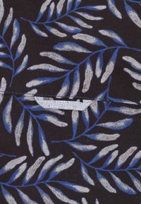 Zwarte stof met een wit en blauw bladerenpatroon. Een klein wit label is gedeeltelijk zichtbaar langs de naad. Zachte textuur.