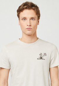 Lichtbeige t-shirt van zacht katoen. Heeft korte mouwen, een ronde hals en een cartoonprint op de linkerkant van de borst met "CHERRY ON TOP."