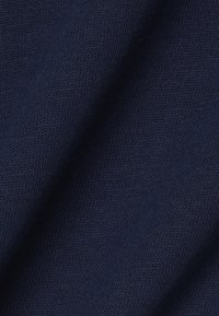 Close-up van donkerblauw gebreide stof met fijne geribbelde textuur en subtiele plooien.