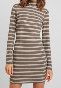 Brązowa sukienka z długim rękawem, prążkowana, z poziomymi białymi paskami, dopasowana w kształcie, z dekoltem typu mock turtleneck. Miękki, teksturowany materiał.