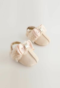 Mocassins pour bébé de couleur beige clair avec des accents en fourrure, un nœud en ruban rayé rose et des coutures décoratives le long du centre. Design en matériau doux.