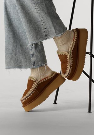 Scarpe platform in suede marrone con bordo a scallop crema, indossate con calze beige a coste e jeans chiari strappati.