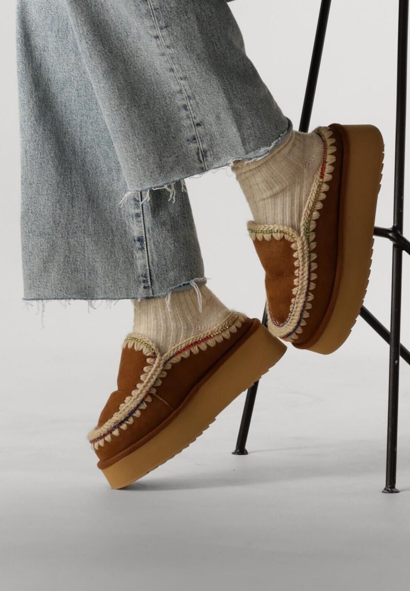 Scarpe platform in suede marrone con bordo a scallop crema, indossate con calze beige a coste e jeans chiari strappati.