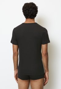 T-shirt noir à manches courtes avec un col rond, texture lisse et design ajusté, vu de dos, associé à un short noir.