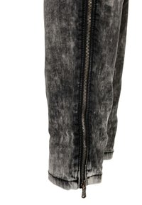 Los pantalones de mezclilla grises presentan un lavado desvanecido y un cierre lateral. La tela tiene una textura suave con un ligero brillo.