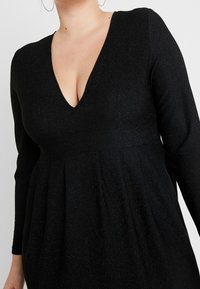 Czarna sukienka z długimi rękawami, głębokim dekoltem w serek, teksturowana tkanina z delikatnym blaskiem oraz dopasowany gorset z plisowaną spódnicą.