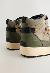 Groene hoge sneakers van een textiele stof, met een verstevigde hak, oranje accenten en een crèmekleurige rubberen zool. Bevat een rits en banden.