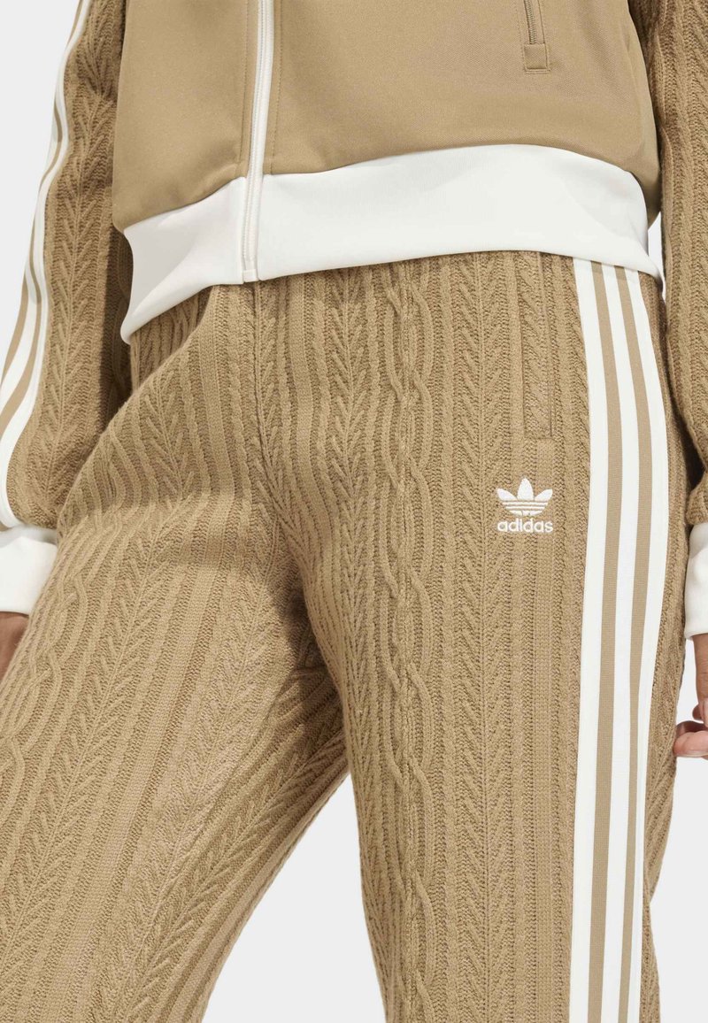 Tan Adidas tracksuit featuring textured cable knit pattern on pants, white stripes along the sides, and a white ribbed waistband.