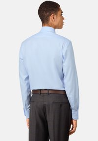 Vaaleansinisessä, istuvassa pussipaidassa on nappiresorit ja klassinen kaulus, jotka on yhdistetty tummansuklaanharmaisiin housuihin ja ruskeaan vyöhön.