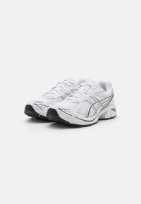 Hvite joggesko med mesh-overside, snøring, sølvdetaljer og en slitesterk svart gummisåle med mønstrete grep.