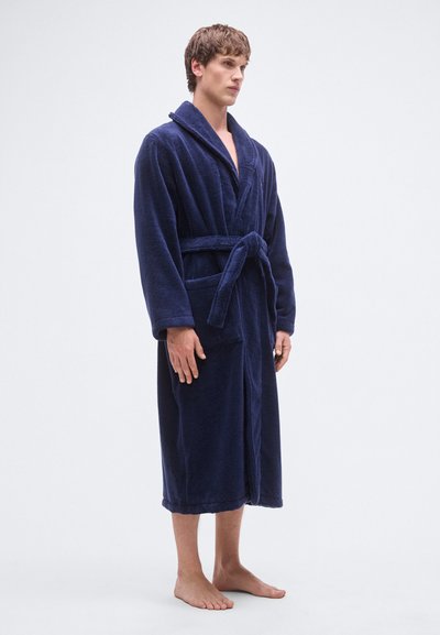 Marineblå badekåpe laget av mykt, teksturert stoff. Har sjalskrage, innsvingt midje med belte og to fremre lommer. Lange ermer og knelengde.
