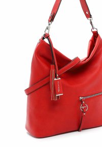 Sac bandoulière en cuir rouge avec poche zippée à l'avant, sangle réglable et pompon décoratif attaché à une pièce métallique.