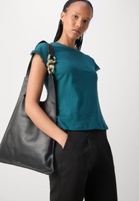 Teal bomull T-skjorte med blondekant på ermene, parret med en svart skinn totebag med gullkjedeaccent. Svart bukse.