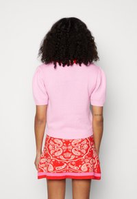 Rosa stickad kortärmad topp med puffärmar, ihop med en röd kjol med paisleymönster som har en rosa kant och subtil textur.