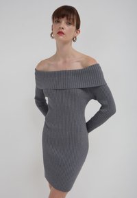 Graues, geripptes Strickkleid mit schulterfreiem Ausschnitt, langen Ärmeln und figurbetonter Silhouette. Die Textur ist weich und dehnbar.