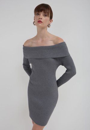 Robe-pull grise à côtes avec un décolleté dénudé, des manches longues et une silhouette ajustée. La texture est douce et extensible.