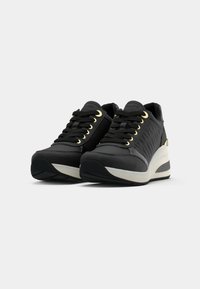 Black sneakers with quilted sides, gold eyelets, black laces, and white wedge soles positioned on a white background.