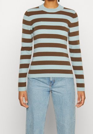 Personne portant un pull en maille ajusté à manches longues avec des rayures horizontales marron et bleu clair, associé à un jean bleu clair.