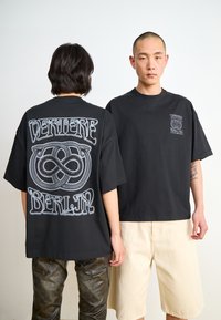Black oversized t-shirt featuring a silver graphic design on the back and a small logo on the front, made of soft cotton fabric.