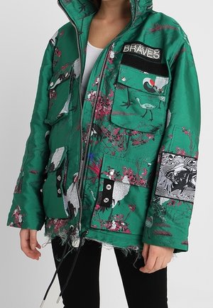 Veste verte avec imprimés d'oiseaux et de fleurs, plusieurs poches avant, patch noir et blanc sur la manche et texte "BRAVES" sur la poche poitrine.