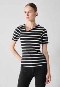 Black and white striped short-sleeve top with a v-neck design and soft fabric. Paired with black pants, highlighting the top's shape.