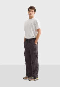 Svarta cargo byxor med flera fickor, dragsko i midjan och ett lappdetalj. Kombinerat med en enkel vit t-shirt med kort ärm och färgglada skor.