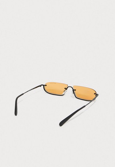 Lunettes de soleil avec monture noire en métal et verres rectangulaires orange. Des branches fines relient les verres, dotées d'un design minimaliste et de touches subtiles.