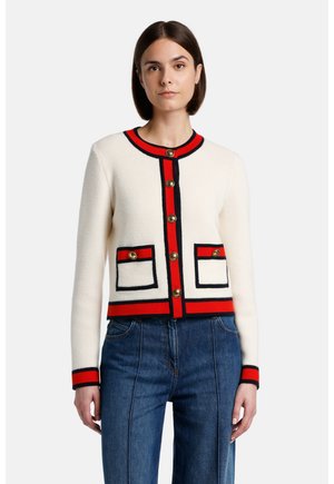 Cardigan blanc tricoté avec des rayures rouges et bleues, boutons dorés et deux poches avant bordées de bleu marine. Manches longues avec des poignets côtelés.