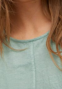 Haut vert menthe avec un col ronde, en tissu texturé et un design simple. Présente un détail de couture subtil au centre devant.