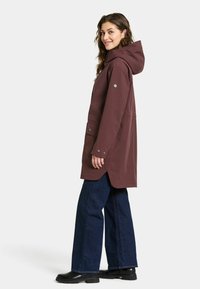 Bordeaux waterdichte parka met een capuchon, twee voorzakken en drukknopen, gecombineerd met donkerblauwe wijde jeans en zwarte laarzen.