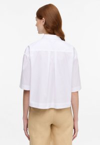 White cropped shirt with short sleeves, featuring a classic collar and back yoke detail, made from smooth, lightweight fabric.