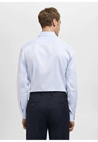 Svetlomodra srajca z dolgimi rokavi in tradicionalnim ovratnikom, gladke teksture, z zapetimi manšetami, v kombinaciji s temnimi hlačami z zadnjimi žepi.