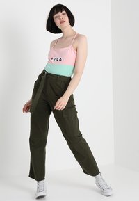 FILA fargeblokket tanktopp i rosa og mint med logo; kombinert med olivenfargede cargobukser med flere lommer og belte. Hvite joggesko.