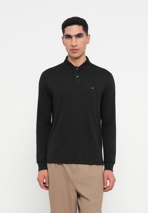 Zwarte polo met lange mouwen, drie knopen, geribbeld kraagje en kleine logo-accent aan de linker borstzijde. Fijne textuur.