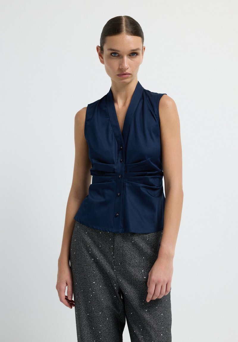Top senza maniche navy con scollo a V e parte frontale arricciata, caratterizzato da bottoni al centro e una texture liscia.