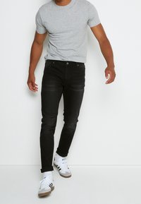 Svarta denimjeans med slim fit, med femficksdesign och kontrasterande sömmar, ihopparat med en ljusgrå t-shirt med rund hals och vita sneakers.