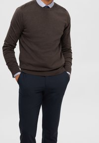 Brunstickad tröja med rund halsringning, ribbade muddar, kombinerad med marinblå byxor. Tröjan har en slät yta och slim fit.