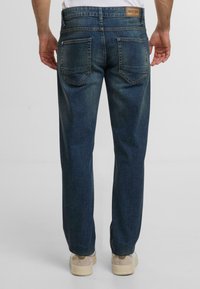 Jeans in denim blu scuro con una vestibilità a gamba dritta, due tasche posteriori e un'etichetta in pelle in vita. Il tessuto ha una texture liscia.